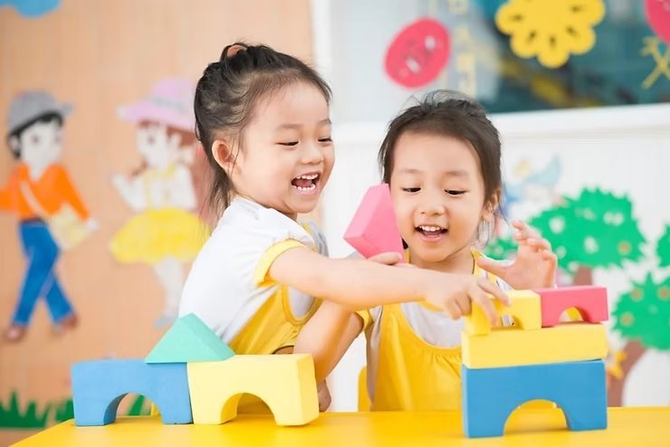 2 young girls with black hair playing with blocks in a school or daycare environment