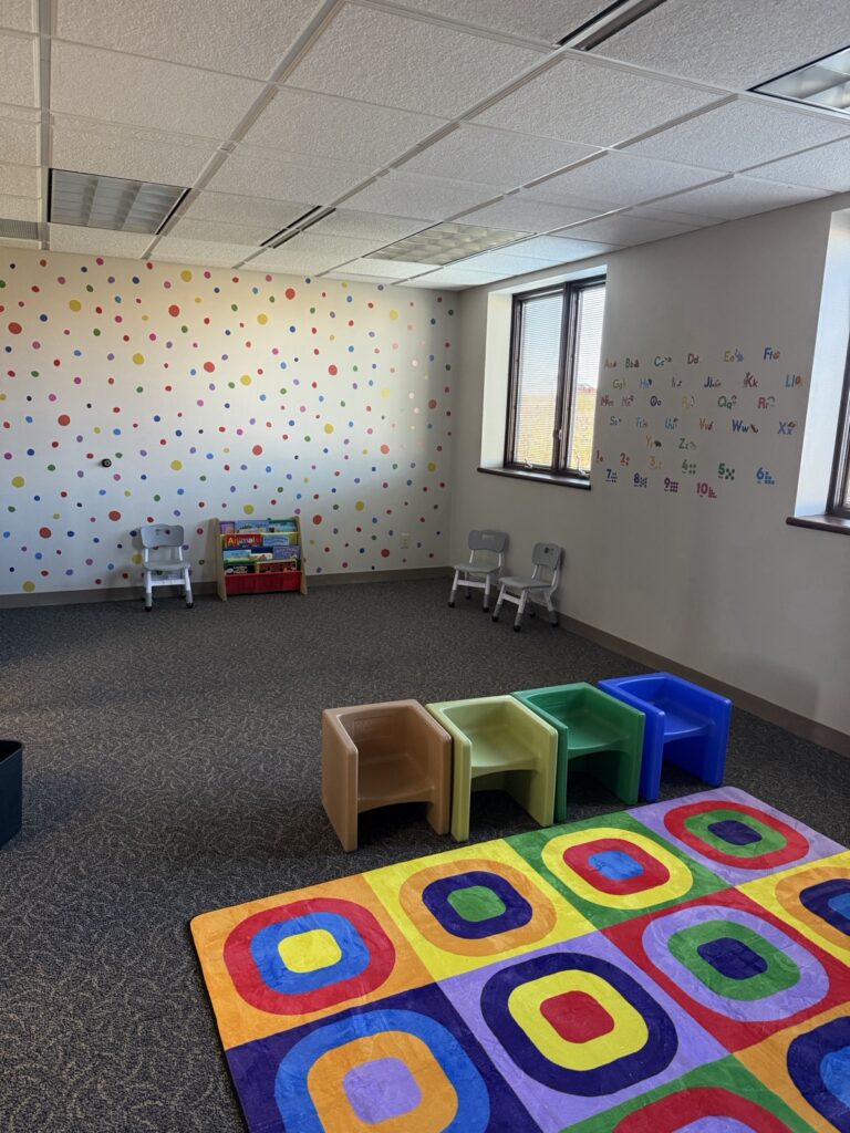 Therapy room with a polka-dot wall, colorful cube chairs and a patterned play rug