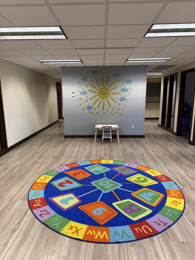 Bright open play area with a sun mural and colorful alphabet rug at Ignite Child Development Services